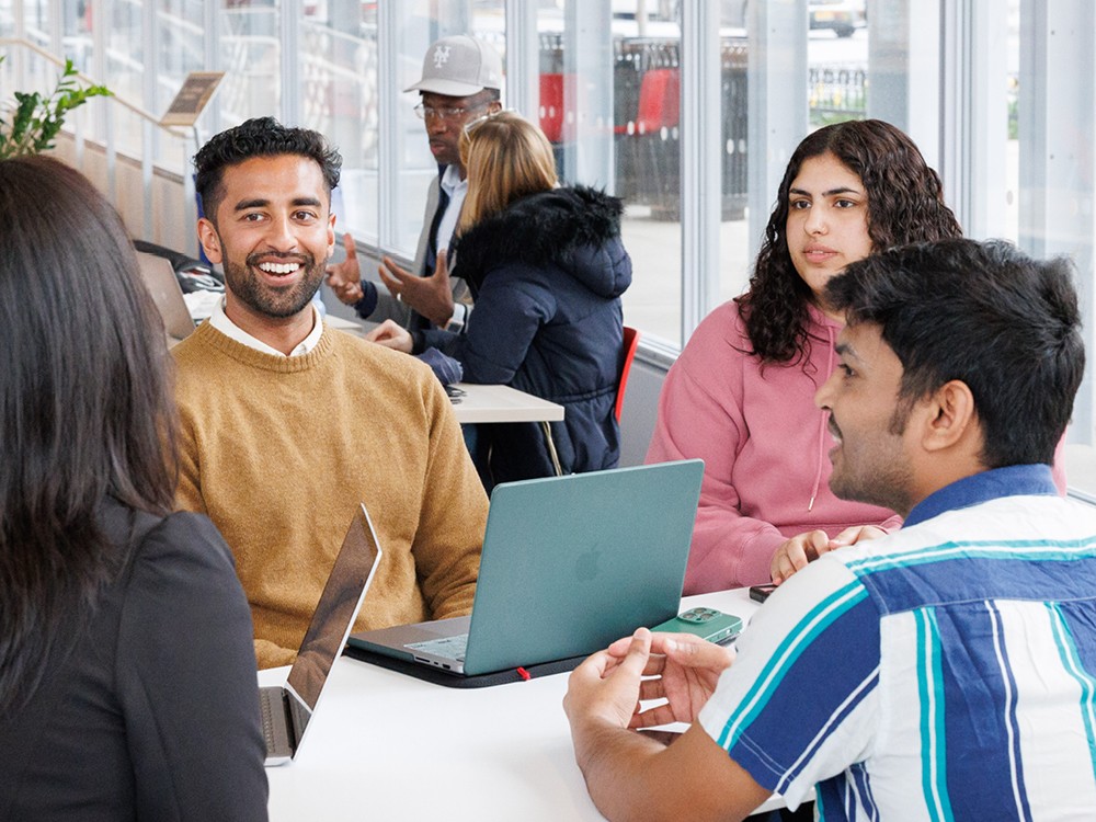 Four students sitting in a group with laptops on table