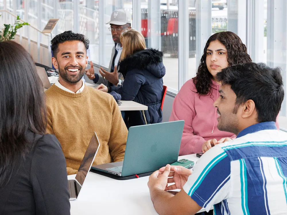Four students sitting in a group with laptops on table