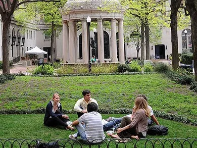 Students sitting on a campus lawn with buildings in the background
