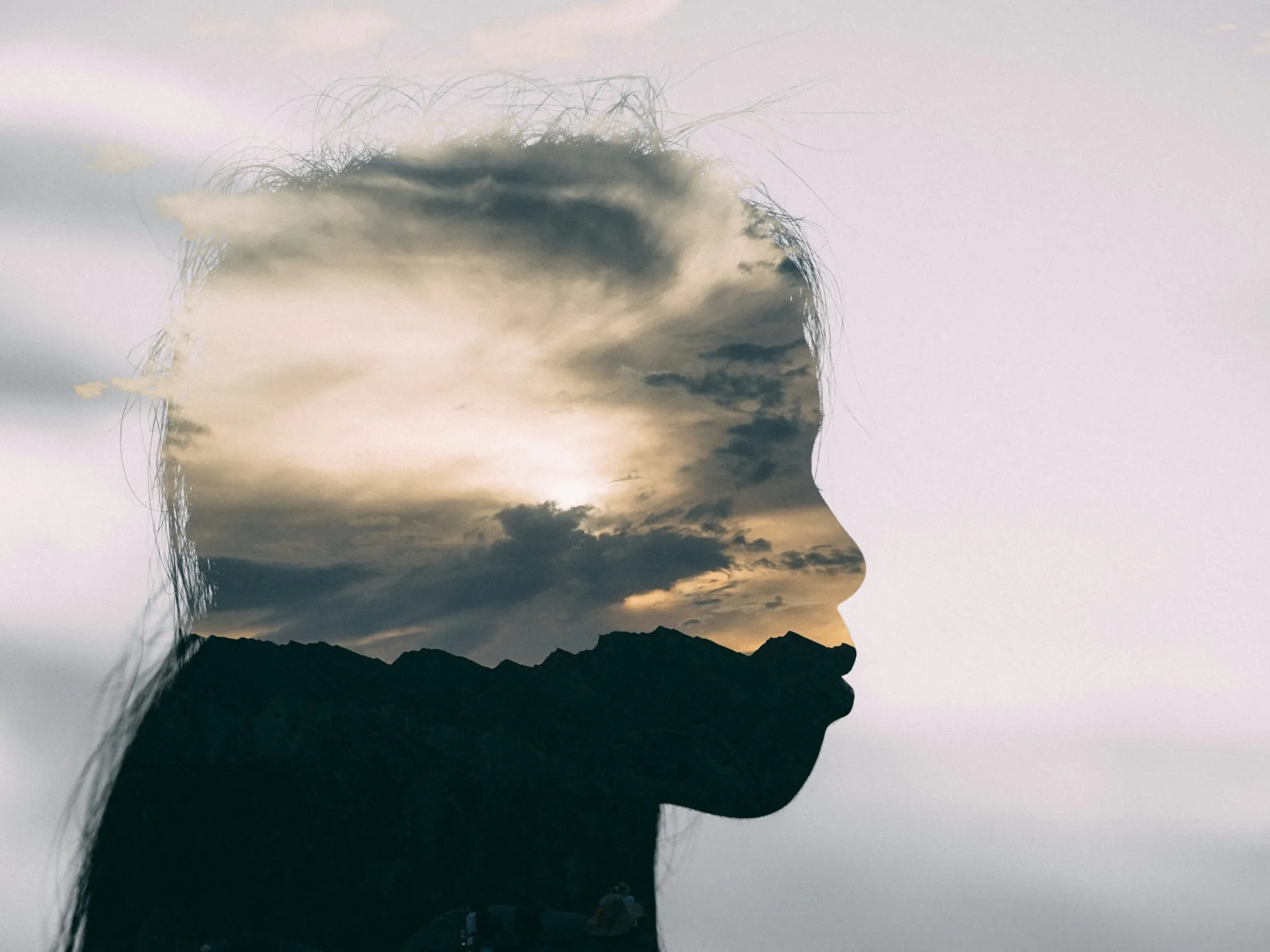 Silhouette of a person with an overlay of a cloudy sky with sun peeking through the clouds