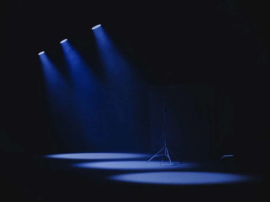 Three blue spot lights cast pool of light on black stage