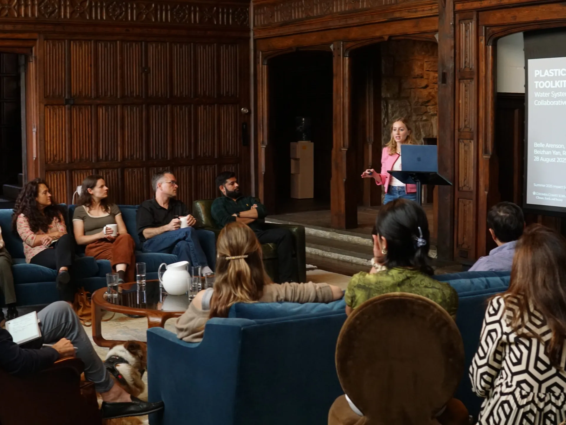 Group of people sitting in a large wood-paneled room attending a presentation