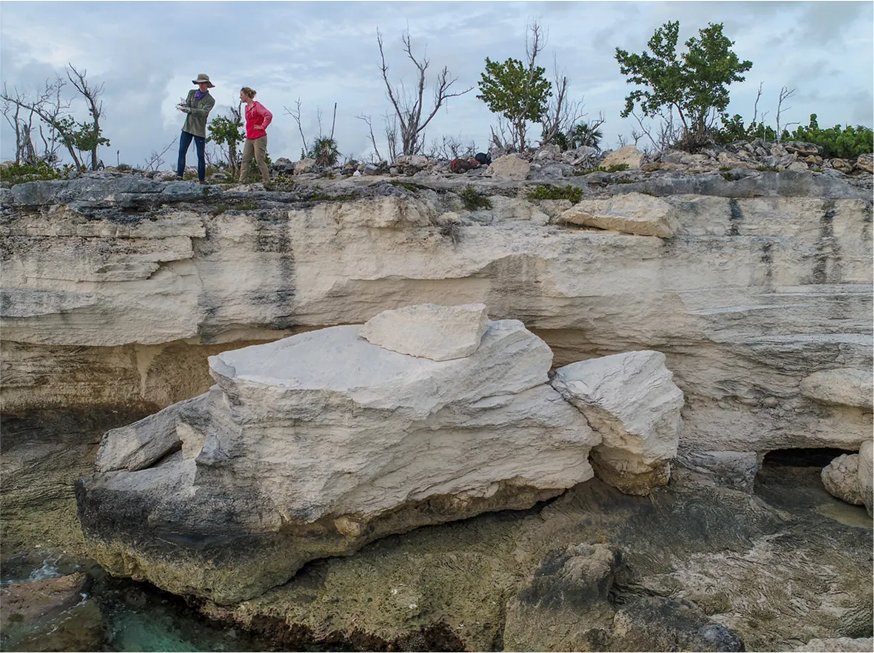 Two people standing on a rock formation over the water 