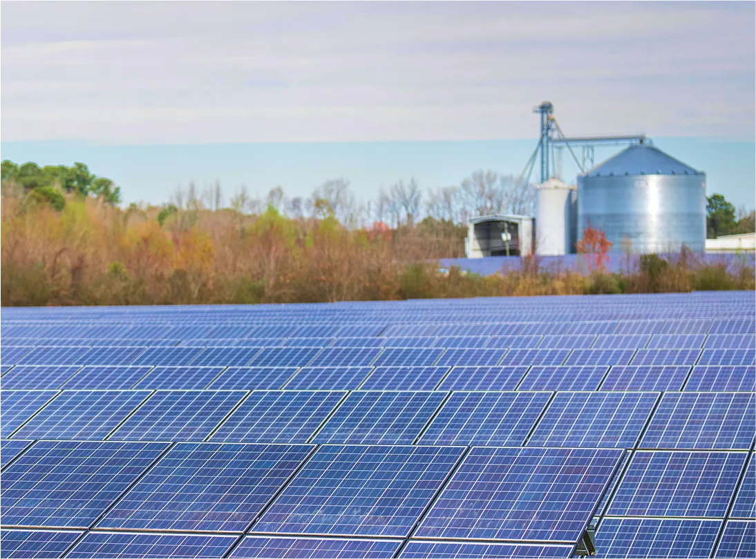 Solar panels with farming silo and trees in the background