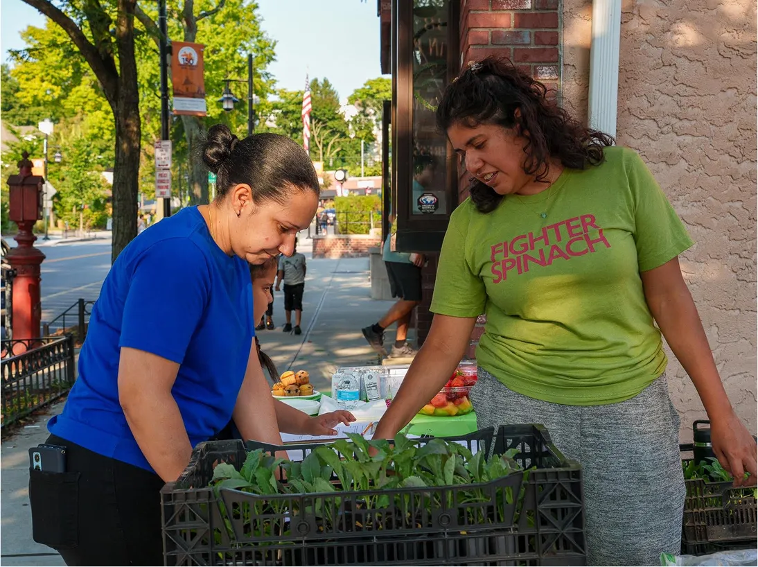 Two people at a table with vegetable plants on a New York City street