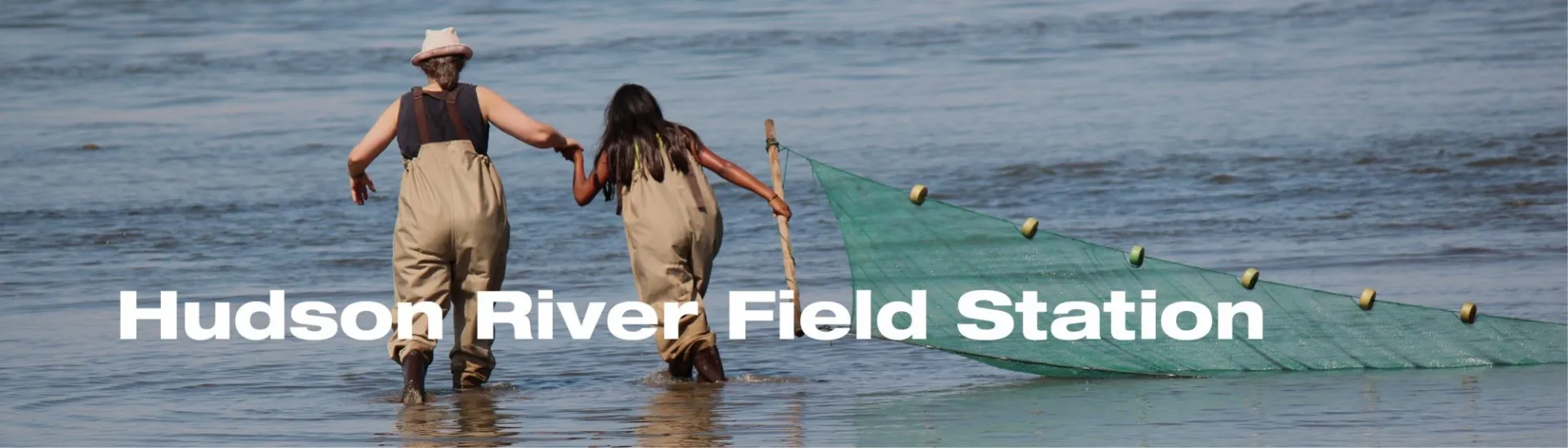 Picture of two women in a river holding a net that reads "Hudson River Field Station"